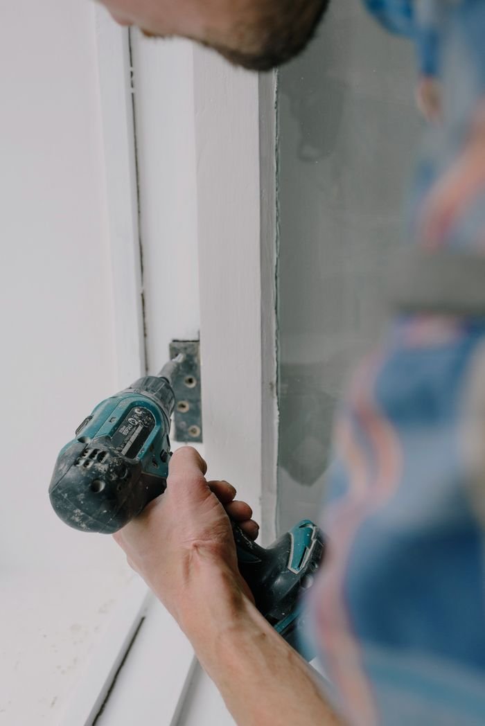 Services Crop bearded guy installing new wooden window with contemporary screwdriver and metal hinge during renovation process in apartment